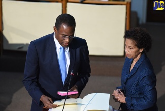 New Member of Parliament for North West St. Andrew, Dr. Nigel Clarke (left), takes the Oath of Office during the sitting of the House of Representatives on March 8. At right is Clerk to the Houses of Parliament, Mrs. Heather Cooke.