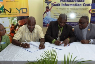 Registrar at the Office of the Children’s Registry (OCR), Greig Smith (2nd right); and Chief Financial Officer of Cabletron Network Systems Limited, Richard Perry (2nd left), sign a Memorandum Of Understanding (MoU) for the airing of Ananda Alerts by the cable provider. The signing took place on April 30, at the National Centre for Youth Development (NCYD) in Savanna-la-Mar. Looking on are Parish Coordinator for Disaster Preparedness at the Westmoreland Parish Council, Hilma Tate (left); and Custos of Westmoreland, Hon. The Very Reverend Canon Hartley Perrin.