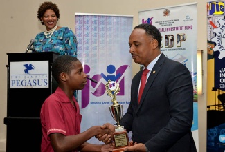 Managing Director of the Jamaica Social Investment Fund (JSIF), Omar Sweeney (right, presents grade-six student at Lethe Primary in St. James, Dontay Scott, with the first-place trophy in the individual performance category of the Jamaica Social Investment Fund’s (JSIF) Integrated Community Development Project (ICDP) School Science Quiz Competition. Looking on is media personality and master of ceremonies, Dahlia Harris. The award ceremony was held on Wednesday, February 21 at The Jamaica Pegasus hotel in New Kingston. 