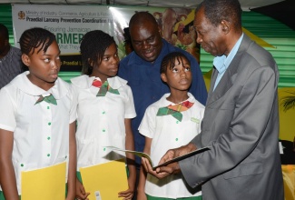 Minister without portfolio in the Ministry of Industry, Commerce, Agriculture and Fisheries, Hon. JC Hutchinson (right), has the attention of students from the Mona Heights Primary School, at the launch of the Praedial Larceny Prevention Unit’s (PLPU)  Essay Competition on April 5,  at the Ministry’s  Hope Gardens headquarters, St. Andrew. Looking on is Permanent Secretary in the Ministry, Donovan Stanberry.