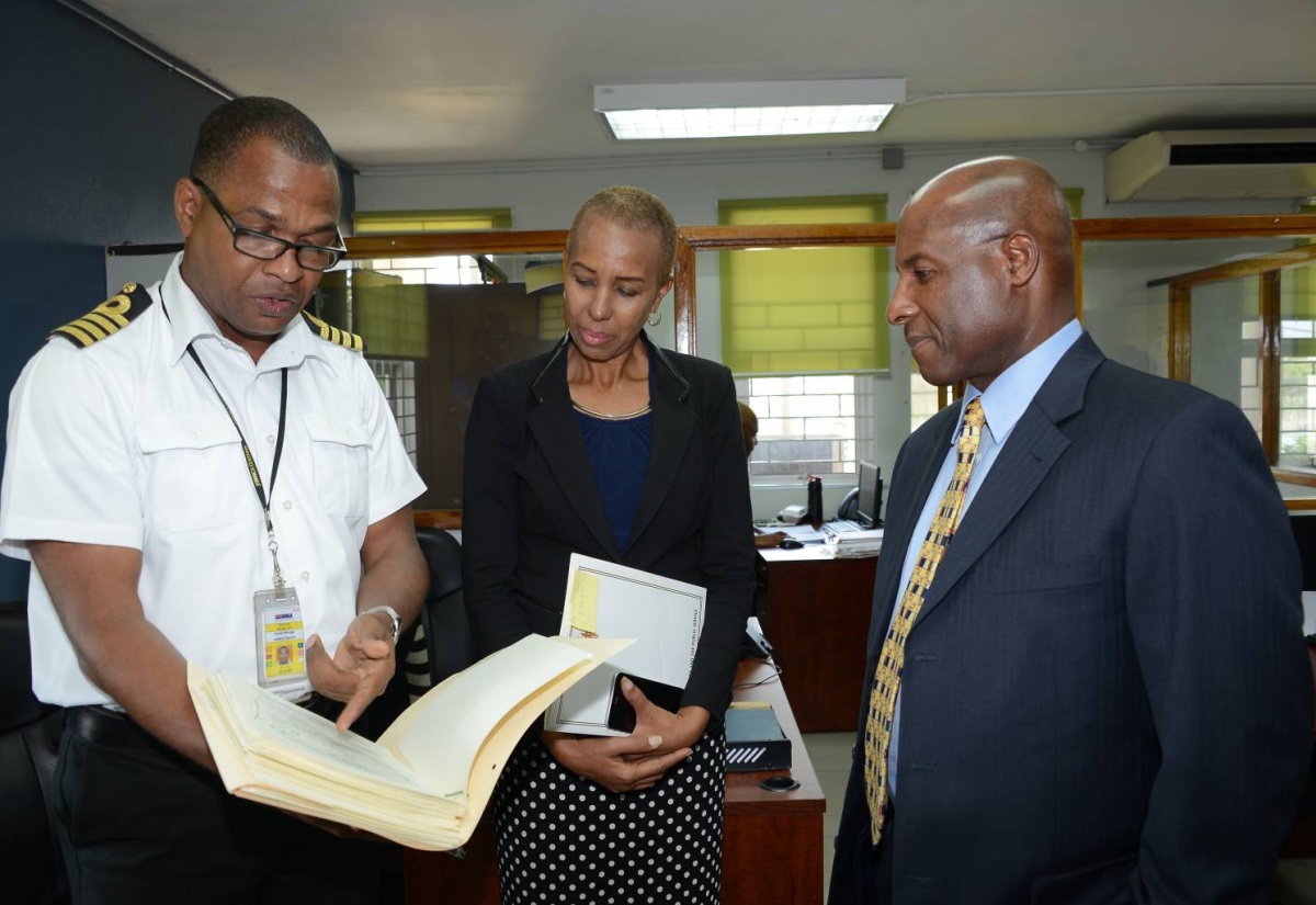 State Minister for Finance and the Public Service, Hon. Fayval Williams (centre), and Senator Aubyn Hill, look at something being pointed out by Chief Invoice Inspector, Jamaica Customs Agency (JCA), Everton Morgan, as he explains the  process of inspection. Occasion was a tour of the JCA, Newport East, Kingston on March 18.