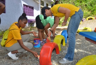 Foreign Affairs and Foreign Trade Minister, Senator the Hon. Kamina Johnson Smith (right), along with resident of Gordon Town in St. Andrew, Renechia Osbourne, paints playground equipment at the Mission House Methodist Basic School in the community during Labour Day activities on Tuesday, May 23.