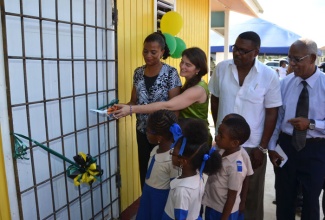 Principal of the Reliance Basic School, in Braeton, St. Catherine, Judith Royal-Gardener (left), and Executive Director at Food For the Poor (FFP) Canada, Samantha Mahfood (second  left), cut the ribbon for the official opening of the new Reliance Basic School, on November 28. Looking on are: Councillor for the Braeton Division, Anthony Wint (third left); former Board Chairman of the school, Owen Saunders on (fourth left), and students.   