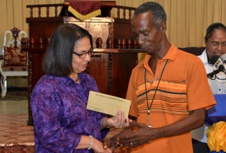 Minister of Labour and Social Security, Hon. Shahine Robinson (left), presents Horace Allen with a relief cheque, at the Linstead New Testament Church of God, in Commodore, St. Catherine, on July 21. Occasion was a ceremony to commence distribution of  the $35 million relief grant for households which were damaged during the recent flood.