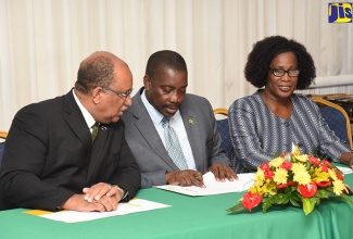 National Security Minister, Hon. Robert Montague (centre), consults with Passport, Immigration and Citizenship Agency (PICA) Chief Executive Officer, Andrew Wynter (left), during PICA's recent swearing-in ceremony for 47 foreign nationals who were granted Jamaican citizenship by the Government. The ceremony was held at the Police Officers' Club in St. Andrew. At right is PICA's Director of Citizenship, Carol Hammond.