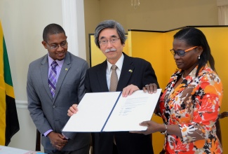 Minister of State in the Ministry of Education, Youth and Information, Hon. Floyd Green (left), observes while Japanese Ambassador to Jamaica, His Excellency Masanori Nakano (centre) and Principal of the Clarendon based Rock River Primary School,  Marcia Ankle, display the agreement for a grant of $10 million, to build a learning centre at the institution. The agreement was signed at the Japanese Embassy, in St. Andrew, on March 22. 