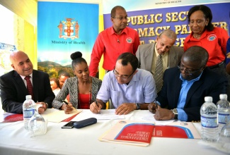 Health Minister, Dr. the Hon. Christopher Tufton (2nd right, seated), and National Health Fund (NHF) Chief Executive Officer, Everton Anderson (right, seated) sign the contract formalising May Pen, Clarendon-based Health First Pharmacy’s participation in the Public Sector Pharmacy Partner Pilot Programme. The signing took place at the pharmacy to launch the initiative, on Monday, December 19.  Looking on (from left, seated) are NHF Chairman, Christopher Zacca; and Health First Pharmacy Managing Director, Oretha Brown. Standing (from left) are Senior NHF Vice President in charge of Information and Communications Technology, Granville Gayle; newly installed Mayor of May Pen, Councillor Winston Maragh; and NHF Vice President in charge of Operations, Ann Logan.