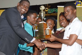 Executive Director of the Scientific Research Council (SRC), Dr. Cliff Riley (left), presents the trophy for the most outstanding tertiary institution  to The Mico University College, at the SRC’ Science and Technology Fair 2016.  The students (from 2nd left) are: Shavaun Blaine, Larey Graham, Monique Reid, Rodaine Hall and John Ross Turnbull. The 2017 event, previously scheduled for April 7, has been postponed.