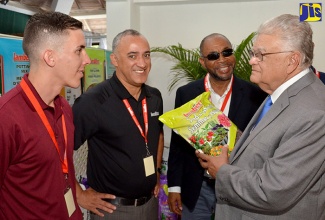 Industry, Commerce, Agriculture and Fisheries Minister,  Hon. Karl Samuda (right), listens as Technical Representative for Canadian entity Lambert Peat Moss Inc., Ramon Alvarado (left), provides details on a bag of plant seeds produced by the company, which was on display during a stakeholder seminar at Caymanas Golf and  Country Club in St. Catherine on Tuesday, September 20. The seminar was jointly staged by Lambert Peat and Jamaica Floral Products Limited/Evergrow Garden Centre under the theme ‘High Quality Growing Media at the Root of High Quality Seedling Growth and Crop Production’. Also listening (from 2nd left) are Lambert Peat’s International Sales Manager, Richard De Quesada; and Jamaica Floral Products Limited/Evergrow Garden Centre General Manager, Burrell Scarlett.