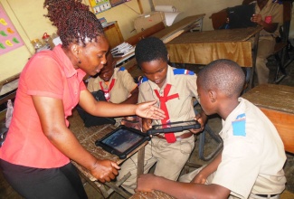 Grade three teacher at the Sir Clifford Campbell Primary School, Karine McIndoe (left), assists two of her students as they familiarize themselves with the new tablet computers that they received during a distribution exercise on October 24, at the school in Savanna-la-Mar, Westmoreland.