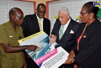 Minister of Transport and Mining, Hon. Mike Henry (second right), and  (from left) Director of the Road Safety Unit in the Ministry, Kenute Hare; Chief Technical Director in the Ministry of Industry, Commerce, Agriculture and Fisheries, Stephen Wedderburn; and Executive Director of the Bureau of Standards Jamaica (BSJ), Yvonne Hall, examine a poster for a road traffic safety standard, JS ISO 39001, which was  launched at the agency’s offices on Winchester Road in Kingston, on September 21