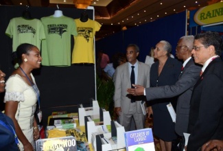 Minister of Foreign Affairs and Foreign Trade, Senator the Hon. A.J Nicholson (2nd right), engages a booth owner (left), during a tour of the Diaspora Marketplace, a new feature of the 5th Biennial Jamaica Diaspora Conference being held at the Montego bay Convention Centre, in St. James. Looking on are: Chairman of the Jamaica Diaspora Conference Preparatory Committee, Mr. Richard Powell (right); Ms Margaret Jobson, Undersecretary at the Ministry of Foreign Affairs and Foreign Trade (2nd left) and Permanent Secretary in the Ministry of Foreign Affairs and Foreign Trade, Ambassador Paul Robotham.