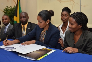 Minister of Youth and Culture, Hon. Lisa Hanna (centre) signs a Memorandum of Understanding (MoU), aimed at enhancing the Ananda Alert System through a multisectoral approach, at the Courtleigh Hotel and Suites in Kingston on May 14, 2014. Others (from left) are: Director, National Intelligence Bureau, Jamaica Constabulary Force (JCF), Superintendent Kirk Ricketts; Registrar, Office of the Children’s Registry (OCR), Greig Smith; former OCR Child Ambassador - Region One, Ashlie Barrett; and Special Projects Manager, Jamaica Information Service, Andrine Davidson. 