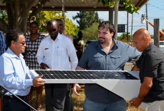 Local Government and Community Development Minister, Hon. Noel Arscott (left), is presented with a solar powered light emitting diode (LED) panel, manufactured by United Stated-based technology solutions firm, Green Energy RG LLC, by Managing Director, Alfred Heyer (centre, foreground); and President, Green Energy RG Caribbean Limited, Jonathan Burke (right), in a symbolic handing over which took place during Tuesday’s (January 8) ceremony at Osbourne Store, Clarendon, to launch the government’s energy saving project, being implemented in local government facilities. The initiative will commence with a pilot phase in Clarendon, and sections of Kingston, St. Andrew, and St. Catherine. Looking on (in background, from left) are: Councillor for the Toll Gate Division of the Clarendon Parish Council, Godfrey Knight; Council Chairman and May Pen Mayor, Scean Barnswell; and Councillor, York Town Division, Liphel Purcell.    