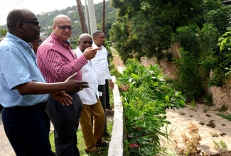 State Minister for Transport, Works and Housing, Hon. Richard Azan (2nd left); North West St. Andrew Member of Parliament, Derrick Smith; and officers of the Ministry view  damage in a section of gully in Meadowbrook, during a tour of the community, on Monday (April 13).