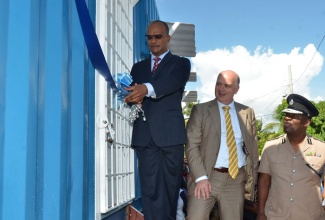 Minister of National Security, Hon. Peter Bunting (left), cuts the ribbon to open a mobile community security and dispute resolution centre, in March Pen, St. Catherine, on November 26. The facility is one of four for the Spanish Town communities of March Pen, Lauriston and Shelter Rock. Looking on are:  Commissioner of Police, Own Ellington (right), and World Bank representative, Giorgio Valentini (centre).