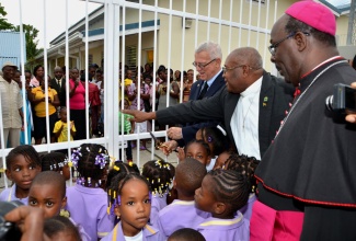 Education Minister, Rev. the Hon. Ronald Thwaites (left), performs the symbolic ribbon cutting exercise to officially open the St. Cyprian’s Early Childhood Institution and Resource Centre, in Highgate, St. Mary, on May 9. Sharing the occasion are: Anglican Suffragan Bishop of Montego Bay, Rt. Rev. Leon Golding (right); Board Chairman of the Institution, Fr. Seymour Hutchinson; and pupils of the school.
