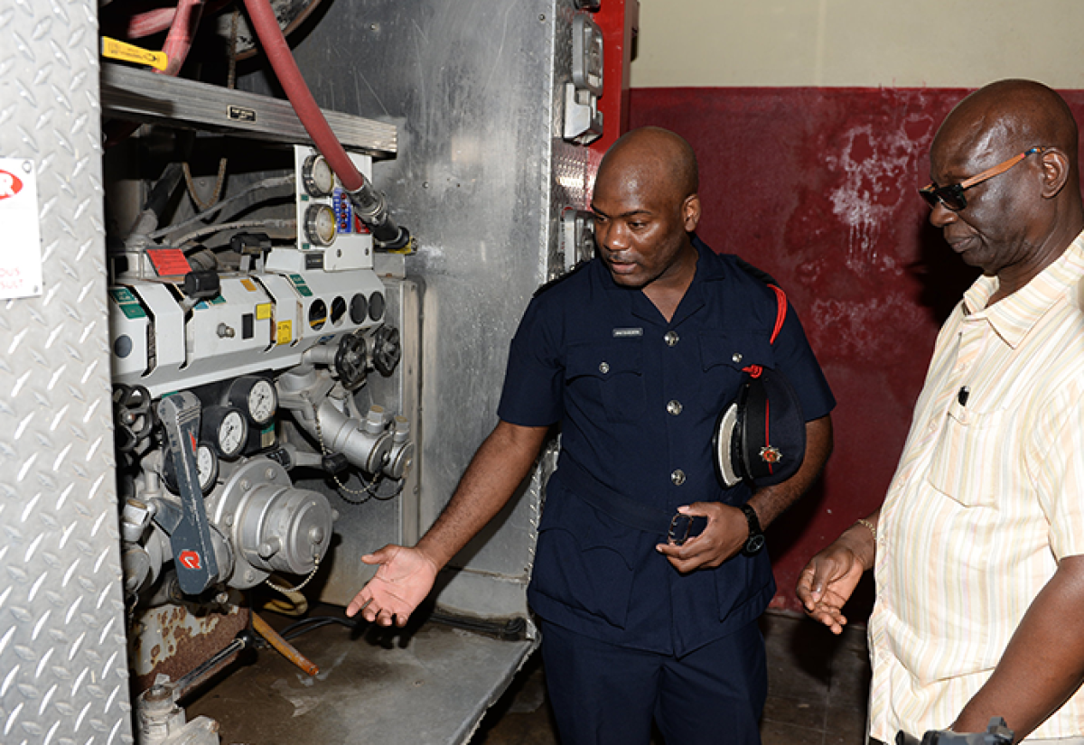 Minister of Local Government and Community Development, Hon. Desmond McKenzie (right), looks on as  Superintendent in charge of the Portland division of the Jamaica Fire Brigade, Windell Patterson, points out a compartment in a fire truck used to service the parish. The Minister recently toured local government facilities in the Portland.