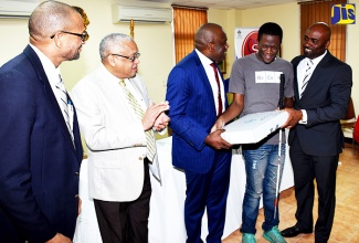 Minister of Science, Energy and Technology, Dr. the Hon. Andrew Wheatley (right), presents a Dell computer to André Fisher (second right), during a handover ceremony at the Centre for Disability Studies, Mona campus, on October 12. Mr. Fisher was among 40 individuals from the community of persons with disabilities who were provided with computerised equipment.  They were provided through the Universal Service Fund. Others sharing in the moment (from left) are Director of Projects, Universal Service Fund, Everold Simms; Principal, University of the West Indies (UWI) Mona, Professor Archibald McDonald; and Director of the Centre for Disability Studies, Senator Floyd Morris.