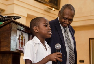 Grade Six student at Rousseau Primary School in Kingston, 11-year-old Te-John Bailey (left), who is the first beneficiary of the Hands Across Jamaica for Righteousness Programme’s Sponsor a Child initiative, speaks during the launch at King’s House, on Friday, September 25 at Kings’ House. Listening keenly is Executive Chairman of Hands Across Jamaica for Righteousness, Evangelist Errol Rattray.