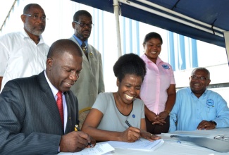  President of the Jamaica Agricultural Society (JAS), Senator Norman Grant (left) and Executive Director of Food For the Poor (FFP), Mrs. Jacqueline Johnson (right), sign agreement for the provision of red peas by the FFP to support the JAS red peas planting project, and to reduce importation of the commodity.  Looking  (from left, standing) are:  First Vice President of the JAS, Donald  Berry;  Second Vice President, Royston Johnson; Agriculture and Fishing Manager, FFP, Selena Ledgister Kellier, and Senior Director, Recipient Services, FFP,  Ron Burgess.  