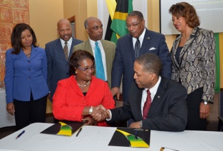 Minister of Industry, Investment and Commerce, Hon. Anthony Hylton (back row, second right), looks on as Senior Vice President, Business Management and Special Projects, Port Authority of Jamaica (PAJ), Beverley Williamson (seated, left), and President and CEO, Paradise Express Ferry, LLC, Garry A. Johnson, shake hands to seal the deal, following the signing of a Memorandum of Understanding on May 6, that will facilitate a ferry service on the north coast. Looking on (from left) are: Assistant Vice President, Business Management and Special Projects, PAJ, Karla Huie; VP Customer Service, Paradise Express Ferry, LLC, Michael Preston; Chairman, Strategic Corporate Interventions Ltd., Christopher Samuda; and JAMPRO’s President, Diane Edwards.