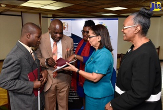 Minister of Labour and Social Security, Hon. Shahine Robinson (second right), listens as Opposition Senator, Dr. Floyd Morris (second left), reads a copy of the Disabilities Act written in Braille. They were at the launch of the Jamaica Council for Persons with Disabilities (JCPD) public education campaign which aims to promote awareness on disability-related matters, the functions of the agency, and the Disabilities Act. The launch was held at the Jamaica Conference Centre, today (November 9). Others (from left) are Member of the Board of Management for JCPD, Alister McLean; Executive Director of the JCPD, Christine Hendricks and Chairman of the Board of Management, JCPD, Dr. Patricia Holness. 