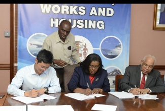 Transport, Works, and Housing Minister, Dr. the Hon. Omar Davies (right); Permanent Secretary in the Ministry, Audrey Sewell (centre); and Deputy General Manager, China Harbour Engineering Company Limited (CHEC), Americas Division, Qiwu Yang, sign copies of the $665.4 million (US$5.53 million) contract to undertake rebuilding of the Kupius Bridge in Pennants, Clarendon, under the Major Infrastructure Development Programme (MIDP). The signing took place at the Ministry’s offices in Kingston on Wednesday, December 16.   Overseeing the proceedings is National Works Agency (NWA) Communications and Customer Service Manager, Stephen Shaw. 