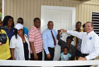 Minister of Labour and Social Security, Hon. Derrick Kellier (centre) presents the keys to a new home to Programme of Advancement Through Health and Education (PATH) beneficiary Joslyn Scott (seated), during the handing over ceremony held on February 7 in Plantations Heights, St. James. Among those sharing the happy moment are Food for the Poor representative, Baldwin Powell (right); Mayor of Montego Bay, Councillor Glendon Harris (5th left); Advisor to the Minister, Phyllis Mitchell (4th left).