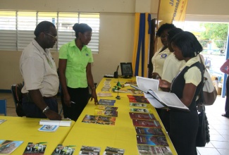 Students of the Moneague Colleague examine reading material at the Jamaica Information Service (JIS) booth, at the book fair hosted by the institution on Thursday, September 12, at its St. Ann campus. JIS staff members Kavannaugh Campbell (left) and Ann Marie Whittingham (2nd left) wait to assist.
