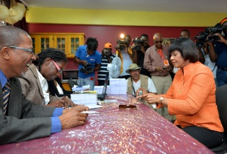 Prime Minister the Most Hon. Portia Simpson Miller (seated, right), counts her $3,000  which she is about to hand over as her nomination fee as a candidate for the constituency of South Western St. Andrew in the February
25 general election, at the Greenwich Town All Age School in Kingston, Tuesday, February 9.  
