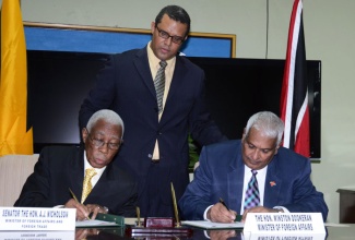 Minister of Foreign Affairs and Foreign Trade, Senator the Hon. A.J. Nicholson (left), and Trinidad and Tobago’s Minister of Foreign Affairs, Hon. Winston Dookeran, sign an agreement outlining the path to be taken in improving free trade and free movement arrangements between the two countries. Observing is Head, Trade Agreements Implementation and Coordination Unit, Ministry, David Prendergast. The agreement was signed at a press briefing held on December 3 at the Ministry’s New Kingston offices, following two days of bilateral talks between the two Ministers. 