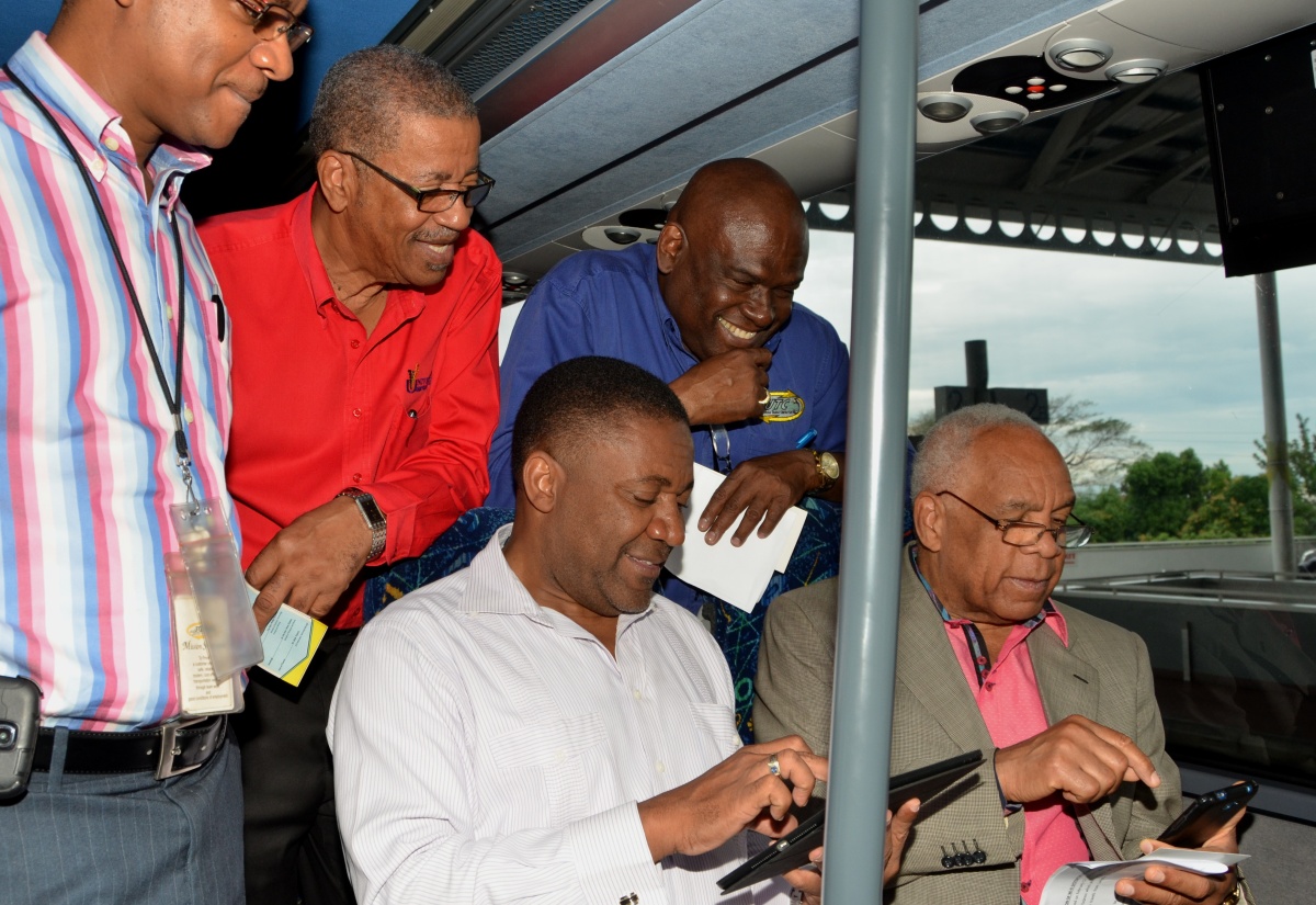 Science, Technology, Energy and Mining Minister, Hon. Phillip Paulwell (left, seated); and Transport, Works and Housing Minister, Dr. the Hon. Omar Davies (right, seated), peruse their mobile devices after accessing the Jamaica Urban Transit Company's (JUTC) Wi-Fi Internet service on one of the state entity's buses, during Friday's (February 12) launch of the Wi-Fi Systems Pilot Project, at the Half Way Tree Transport Centre in St. Andrew. Looking on, from left, are: Manager, Information Technology, JUTC, Brian Tulloch; Chief Executive Officer, Universal Service Fund (USF), Hugh Cross; and JUTC Managing Director, Colin Campbell.