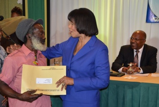 Prime Minister, the Most Hon. Portia Simpson Miller (right), has a special hug and a Certificate of Title for Melbourne Wilson of Creighton Hall, St. Thomas, who  is one of 50 persons who will close out the Jamaica’s Jubilee year mortgage free, under a special debt forgiveness programme called the Jubilee ‘50 for 50’ Housing Initiative, by the Ministry of Transport, Works and Housing. The presentation was made on July 30 at the Knutsford Court Hotel in Kingston.