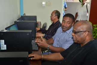 Science, Technology, Energy, and Mining, Hon Phillip Paulwell (centre), explains some of the features on one of 18 computers provided at the newly established Albion Community Access Point Computer Resource Centre at the Social Development Commission's (SDC) office in Montego Bay, St. James, to Deputy Speaker of the House of Representatives and Member of Parliament for Central St. James, Hon. Lloyd B. Smith (right), following the centre's official opening on January 31. Mr. Paulwell was the guest speaker. The centre was outfitted with equipment by the Universal Service Fund (USF), an agency of the Ministry, at a cost $3 million. Also familiarizing himself with one of the computers is Member of Parliament for North West St, James, Dr. Horace Chang.  