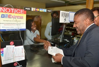 Minister of Science, Technology, Energy and Mining, Hon. Phillip Paulwell (right), greets staff while viewing a receipt for a utility bill that he paid at a Bill Express location at the Central Sorting Office in Kingston, on December 10. Occasion was the official launch of a partnership between Jamaica Post and Grace Kennedy Money Service (GKMS), for the provision of Bill Express services at 39 post offices across the island.