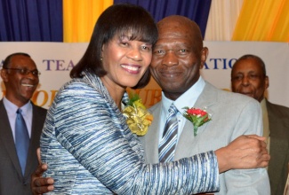 Prime Minister, the Most Hon. Portia Simpson Miller (left), warmly embraces Jamaica Teachers’ Association (JTA) Roll of Honour Awardee 2013, Mr. Patrick Smith, during the presentation ceremony, held at the Jamaica Pegasus Hotel, New Kingston,  on February 12. Sharing in the moment are (back row, from left); 2012 Awardee, Mr. Byron Farquharson,  and JTA Secretary General, Dr. Adolph Cameron. 