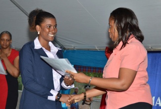 The youngest beneficiary of the Majesty Gardens Phase 1 housing development, Shanika Thompson (left), proudly accepts her keys and package from Social Development Manager at the National Housing Trust (NHT), Wendy- Jo Williams, during the handing over ceremony held on Wednesday, December 18, in the community, located in South West St. Andrew.