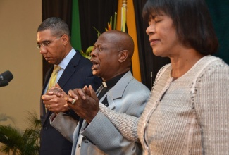 Bishop/Overseer of The Power of Faith Ministries International, Dr. Delford Davis (centre), prays for Prime Minister, the Most Hon. Portia Simpson Miller (right); and Leader of the Opposition, Andrew Holness, during the 34th annual National Leadership Prayer Breakfast held on January 16, at the Jamaica Pegasus Hotel, New Kingston.