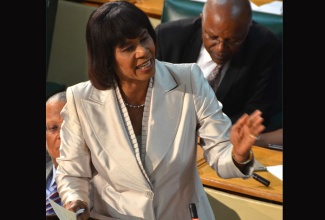 Prime Minister the Most. Hon. Portia Simpson Miller makes a point during her presentation in the 2015/16 Budget Debate, in the House of Representatives on Tuesday, March 24. Mrs. Simpson Miller’s presentation was made under the theme - ‘Moving Forward: Jobs, Growth and Development’.  At left is Minister of Finance and Planning, Dr. the Hon. Peter Phillips and at right is Minister with Responsibility for Housing, the Hon. Morais Guy.