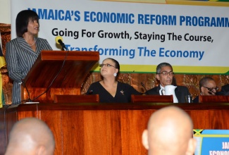 Prime Minister, the Most Hon. Portia Simpson Miller (at podium), delivering the keynote address at Thursday’s (Sept. 12), Economic Reform Programme (ERP) stakeholders conference, hosted by the Ministry of Finance and Planning at the Jamaica Conference Centre, downtown Kingston, under the theme: “Jamaica’s Economic Programme – Going for Growth, Staying the Course, Transforming the Economy”. Also pictured are: Minister with Responsibility for Information, Senator the Hon. Sandrea Falconer (left, seated); and Co-Chairmen, Economic Programme Oversight Committee (EPOC), Richard Byles (2nd right); and Bank of Jamaica (BoJ) Governor, Brian Wynter.