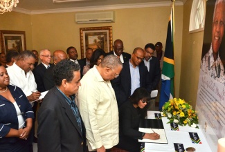 Prime Minister, the Most Hon. Portia Simpson Miller, signing the Condolence Book for the late former South African President Nelson Mandela, at the South African High Commission in St. Andrew on December 6. The Prime Minister is accompanied by Members of the Cabinet who took a break from their two day retreat and travelled to the High Commission where they also signed the Condolence Book.