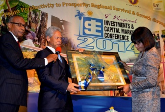 Prime Minister, the Most Hon. Portia Simpson Miller (right), receives a gift from Chairman, Jamaica Stock Exchange (JSE), Donovan Perkins (centre), following her keynote presentation at the opening of the JSE’s Ninth Regional Conference on Investments & Capital Markets on January 21, at the Jamaica Pegasus Hotel in New Kingston. At left is Master of Ceremonies for the evening, Michael Anthony Cuffe.