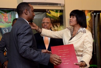 Prime Minister the Most Hon. Portia Simpson Miller (right), moves to embrace President, Jamaica Civil Service Association, Oneil Grant (left), as she hands him a copy of the Heads of Agreement for the 2012-2015 contract period between  the Government of Jamaica and the Public Sector Unions/Associations, which was signed today (March 6), at the Office of the Prime Minister. Looking on is Finance and Planning Minister, Dr. the Hon. Peter Phillips.