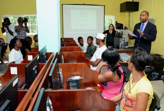 Minister of State in the Ministry of Science, Technology, Energy and Mining, Hon. Julian Robinson (standing right), addresses residents from communities in South East St. Andrew on December 2, who benefitted from hands-on training under the Digital Jam 3.0, the Caribbean Edition programme.  The training was held at the McGregor Gardens Centre.