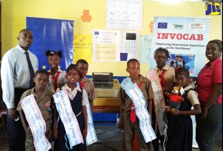 Junior Expert for the Improving Innovation Capacities in the Caribbean (INVOCAB) Project at the Scientific Research Council (SRC), Yanique Wallace (right), shares a photo opportunity with Principal of Bull Bay All-Age, Justin Duncan (left), and students of the school, which won the primary category of the INVOCAB Science and Technology Innovation Competition. Occasion was a ceremony held on September 20 at the St. Thomas-based institution to present the SRC trophy to the school.