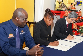 Education, Youth and Information Minister, Senator the Hon. Ruel Reid (left), looks on as Japan’s Ambassador to Jamaica, His Excellency Masanori Nakano (right), and Principal of Middleton Primary School in St. Thomas, Jennifer Crawford, sign an agreement for a $10-million (US$82,214) grant to the institution to construct a canteen. The signing took place at the Ambassador’s Paddington Terrace residence in St. Andrew on March 9. The sum has been provided under the Japanese Government’s Grant Assistance for Grassroots Human Security Projects Programme.  