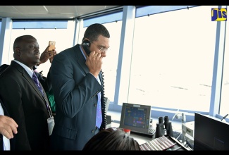 Prime Minister, the Most Hon. Andrew Holness (second left), tests his skills as an air traffic controller by welcoming an American Airline flight to Jamaica. Mr. Holness was on an official tour of the recently commissioned state-of-the-art air traffic control tower at the Norman Manley International Airport (NMIA) in Kingston on April 19. At left is Chief Air Traffic Control Officer at the NMIA, Mark Phillips. 