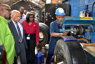 Transport, Works and Housing Minister, Dr. the Hon. Omar Davies (2nd left), and Permanent Secretary, Ministry of Transport, Works and Housing, Audrey Sewell (2nd right), listen, as Jamaica Ultimate Tyre Company Limited (JUTC II) Factory Manager, Hugh Smith (left), explains the tyre retreading process being undertaken by company employee, Ecolas Hughes, during the Ministry officials’ tour of the entity, situated on Maxfield Avenue in Kingston, on June 28, to familiarize themselves with the operations and staff. The entity, which specializes in tyre retreading, repairs and sales, and computerized wheel alignment and balancing of vehicles, is an agency of the Ministry. 