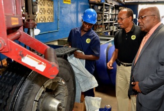 Minister without Portfolio, Ministry of Transport, Works and Housing, Hon. Dr. Morais Guy (right), and General Manager, Jamaica Ultimate Tyre Company (JUTC II), Kenry Jackson (centre), observe as JUTC II retreading technician, Marvin Bennett, carries out repairs on a tyre, during the Minister’s  tour of the Maxfield Avenue-based entity on August 30.